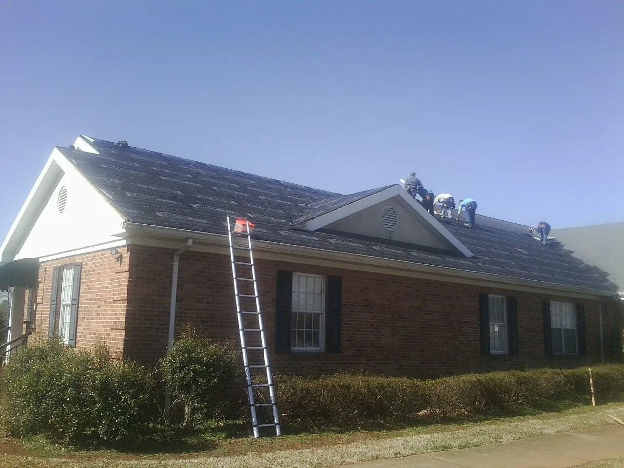 Crew tearing shingles off a brick ranch roof with a ladder set — Emergency Roof Repair work by our crew in Elk Falls
