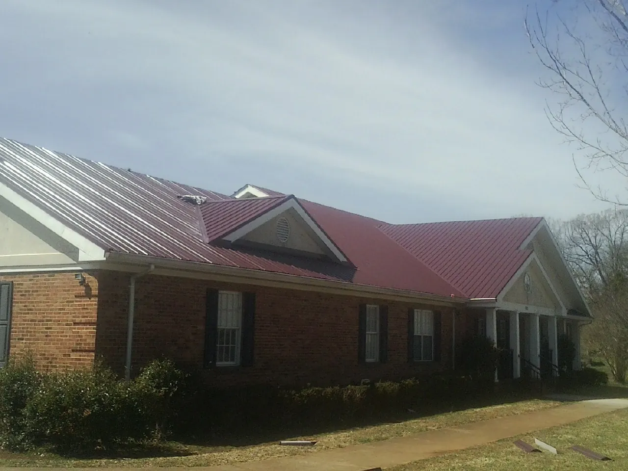 Red metal roof with gabled entries on a long brick building, from a Hail Damage Roof Repair job in Elk Falls