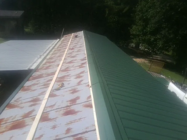 Old rusted panels beside newly installed green metal roofing — Wind Damage Roof Repair by Roofing Brothers in Elk Falls