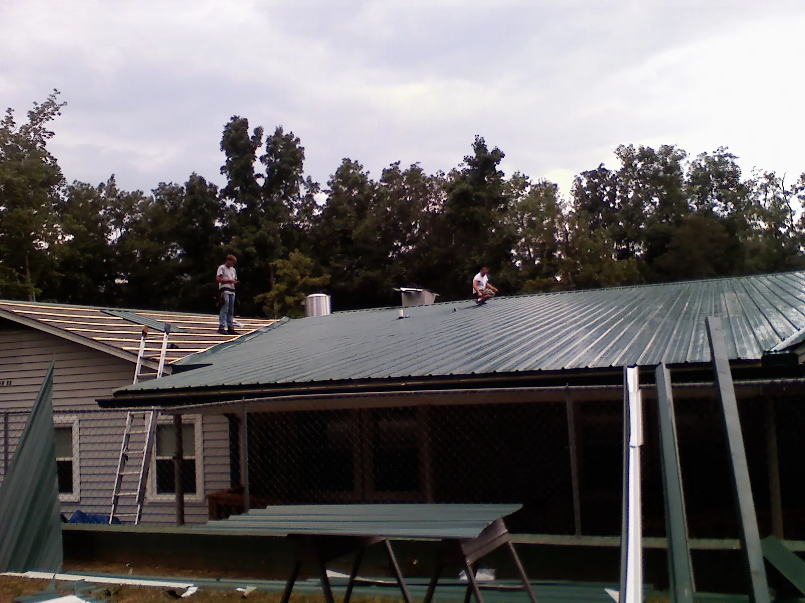 Two roofers installing green metal panels above a covered porch in Elk Falls