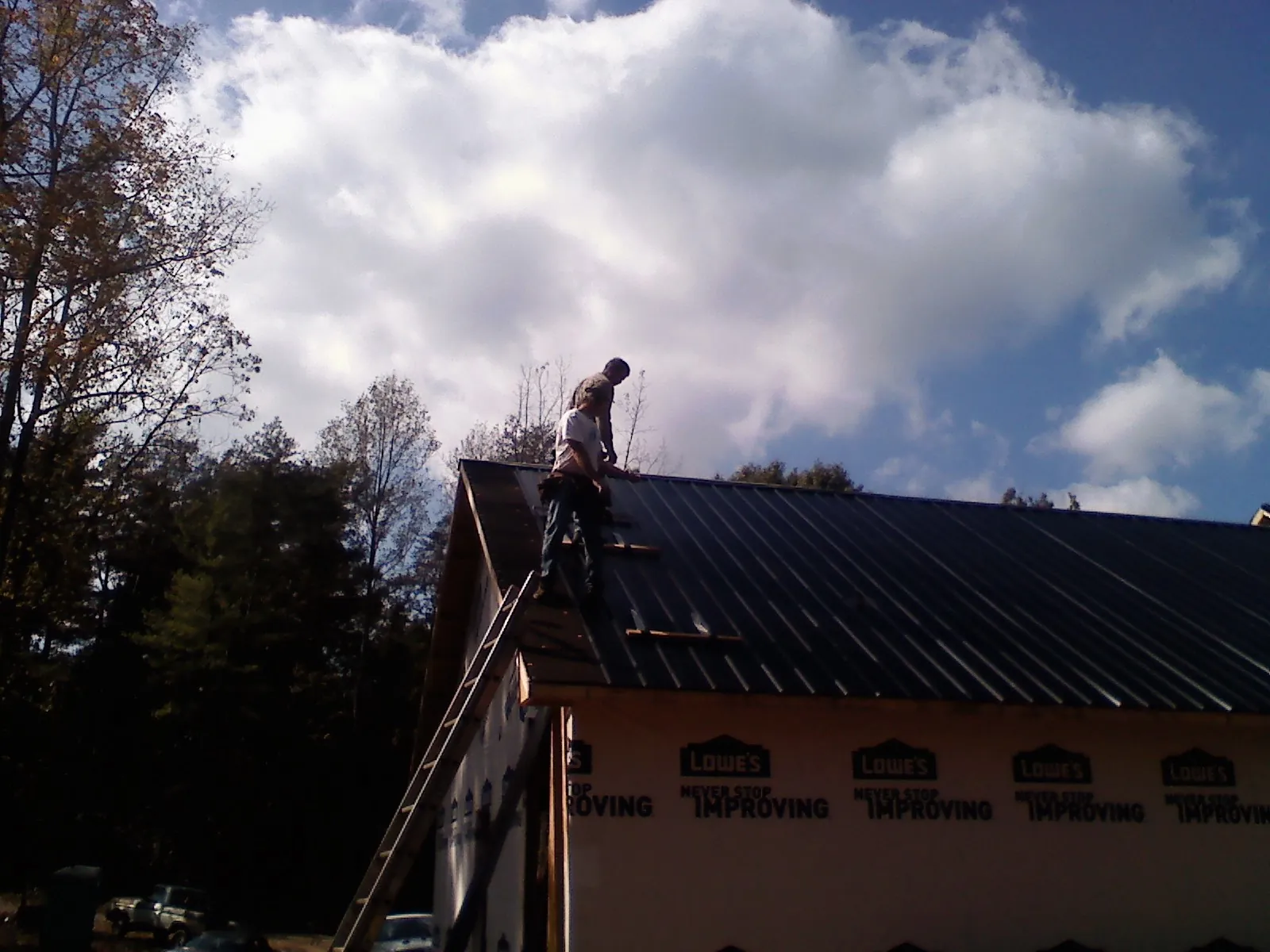 Roofer fastening dark metal panels high against a cloudy sky, from a Roof Inspection job in Elk Falls