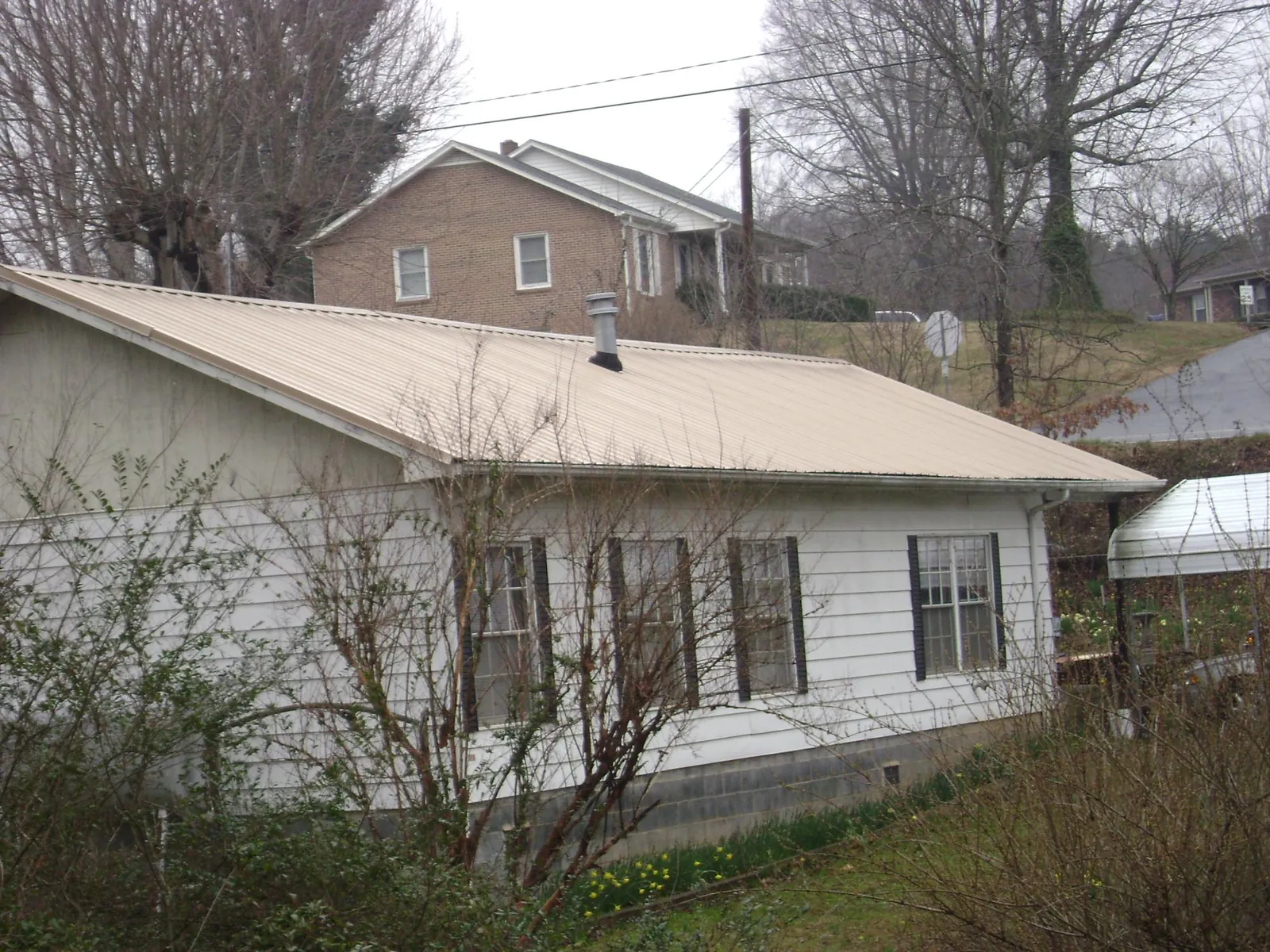 Tan metal roof on a white sided house set into a hillside — Commercial Roofing by Roofing Brothers in Elk Falls