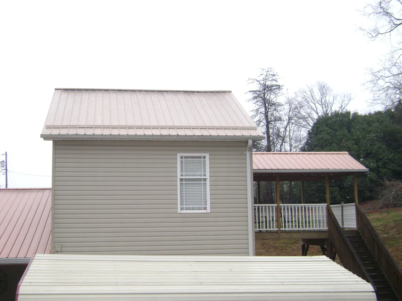 Tan metal roofs on a two story addition and attached porch, from a Roof Replacement job in Elk Falls